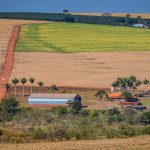 Vista ampla de área rural brasileira com campos, estrada de terra e construções agrícolas.