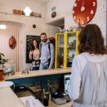 Viajantes são atendidos por funcionários no balcão de recepção de um hostel.