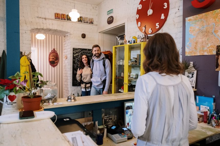 Viajantes são atendidos por funcionários no balcão de recepção de um hostel.