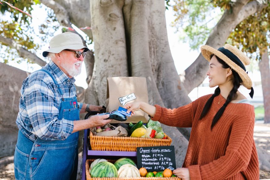Pessoas conversam em uma feira agrícola ao ar livre, com produtos frescos expostos em bancas.