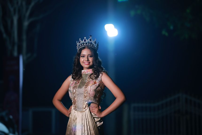 Mulher usando coroa e vestido elegante posa sob iluminação dramática durante a noite