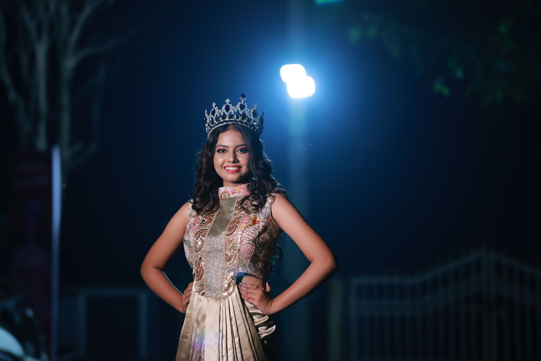 Mulher usando coroa e vestido elegante posa sob iluminação dramática durante a noite