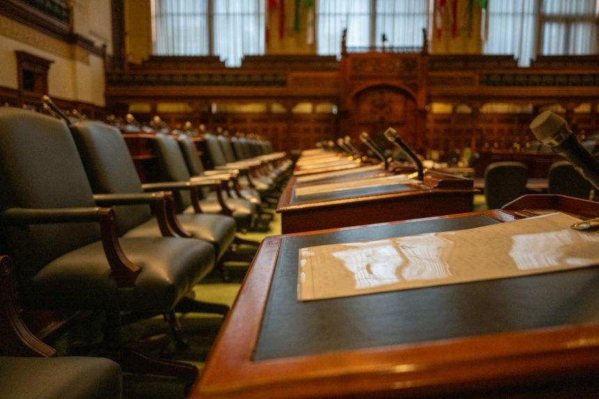 Plenário legislativo vazio, com fileiras de mesas equipadas com microfones.