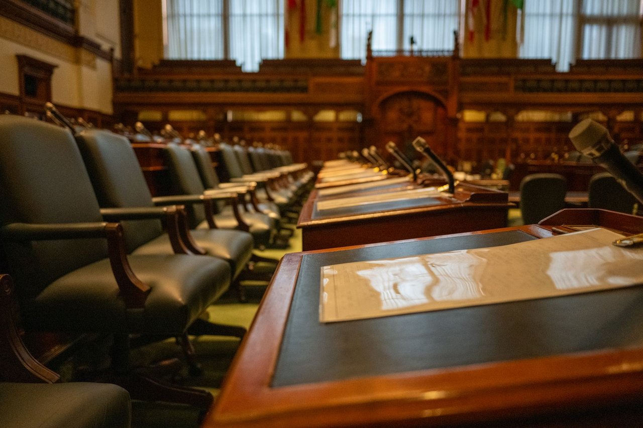 Plenário legislativo vazio, com fileiras de mesas equipadas com microfones.
